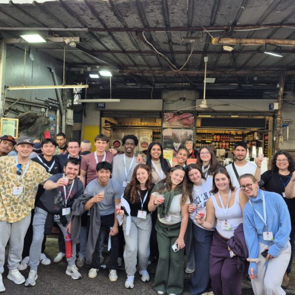 students smiling while holding freshly made smoothies from a stand at the Carmel Market in Tel Aviv, Israel.